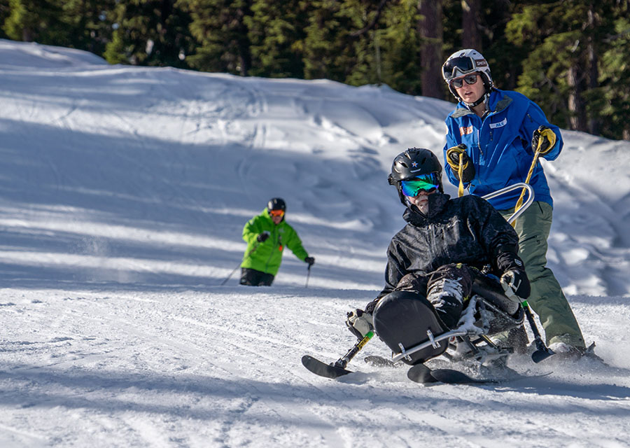 veteran skier in biski tethered by instructor