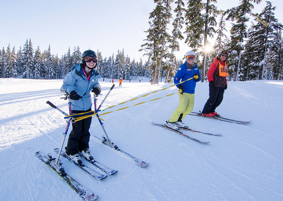 skiier sking on snow slider (walker on skis) with instructor and volunteer