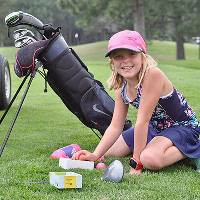 girl kneeling arranging golf balls with clubs in the background