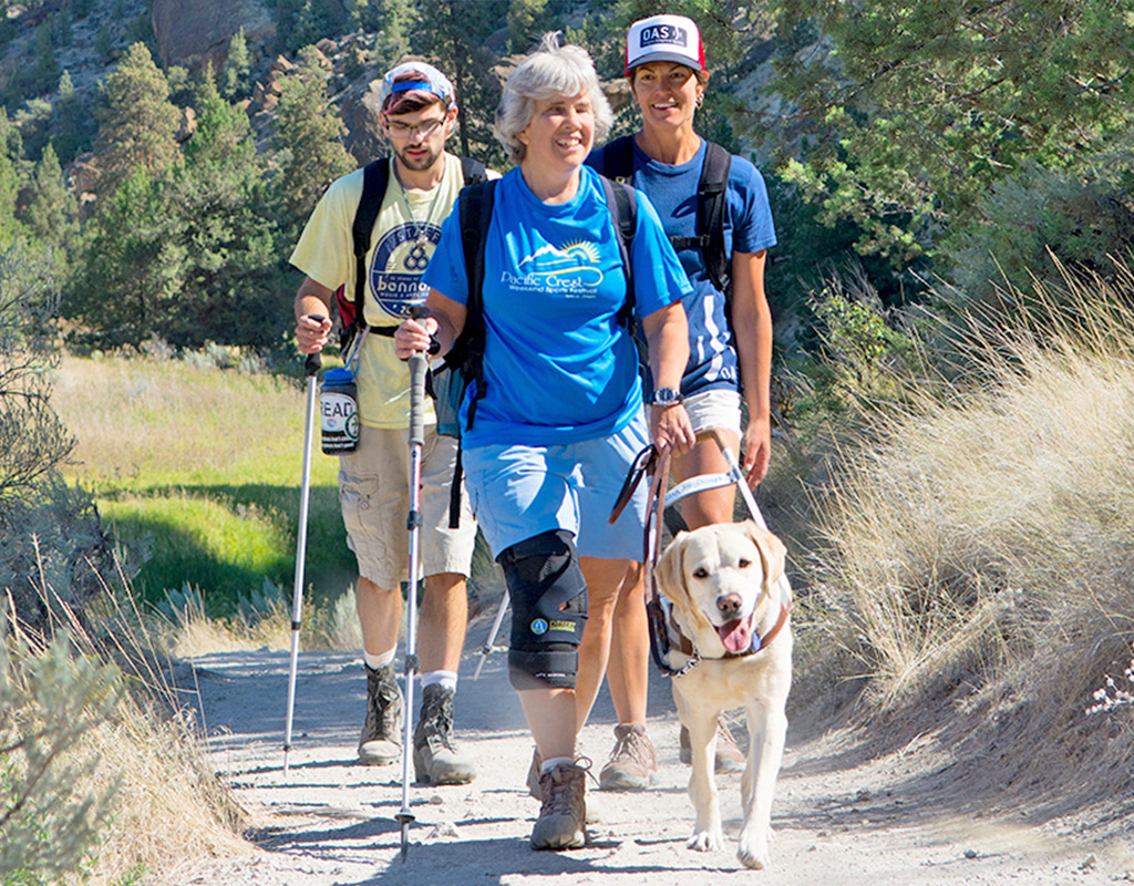female hiker who is blind hiking with her guide dogs and two guides