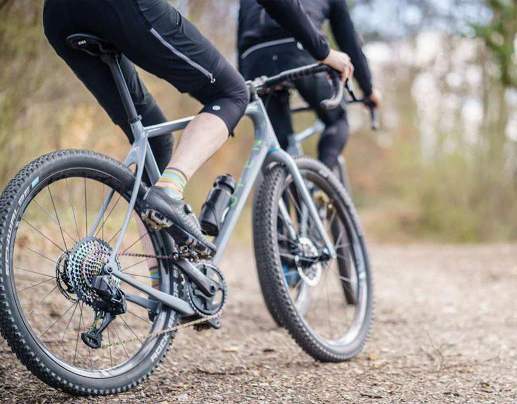 two cyclists on dirt trail, one on OPEN wi.de cycle