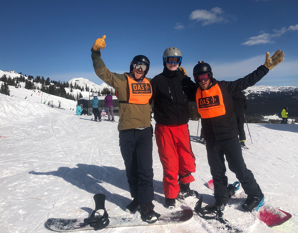 three snowboarders - two volunteers in OAS bibs and one participant doing a classic snowboard bro pose