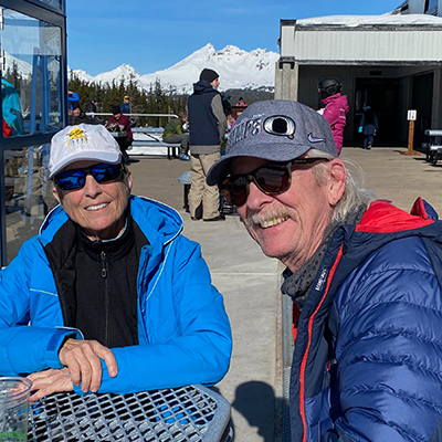 Scott Taylor and wife Lynne, sitting outside, snow capped mountains in background