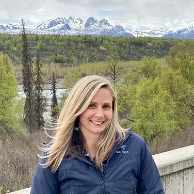 Danielle smiling, facing the camera with snowy mountains in the background