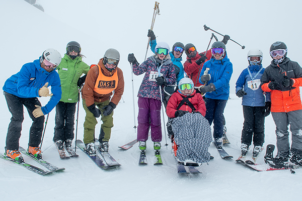 A group of OAS instructors, athletes and volunteers on a snowy slope promoting cheer in their skis, sit-skis and snowboard.
