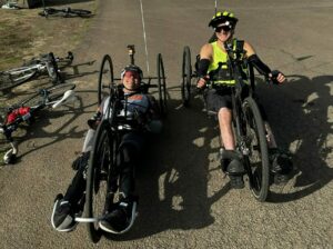 Two adaptive athletes in the bike kits, ready to start cycling for the day on their hand-pedal bikes.