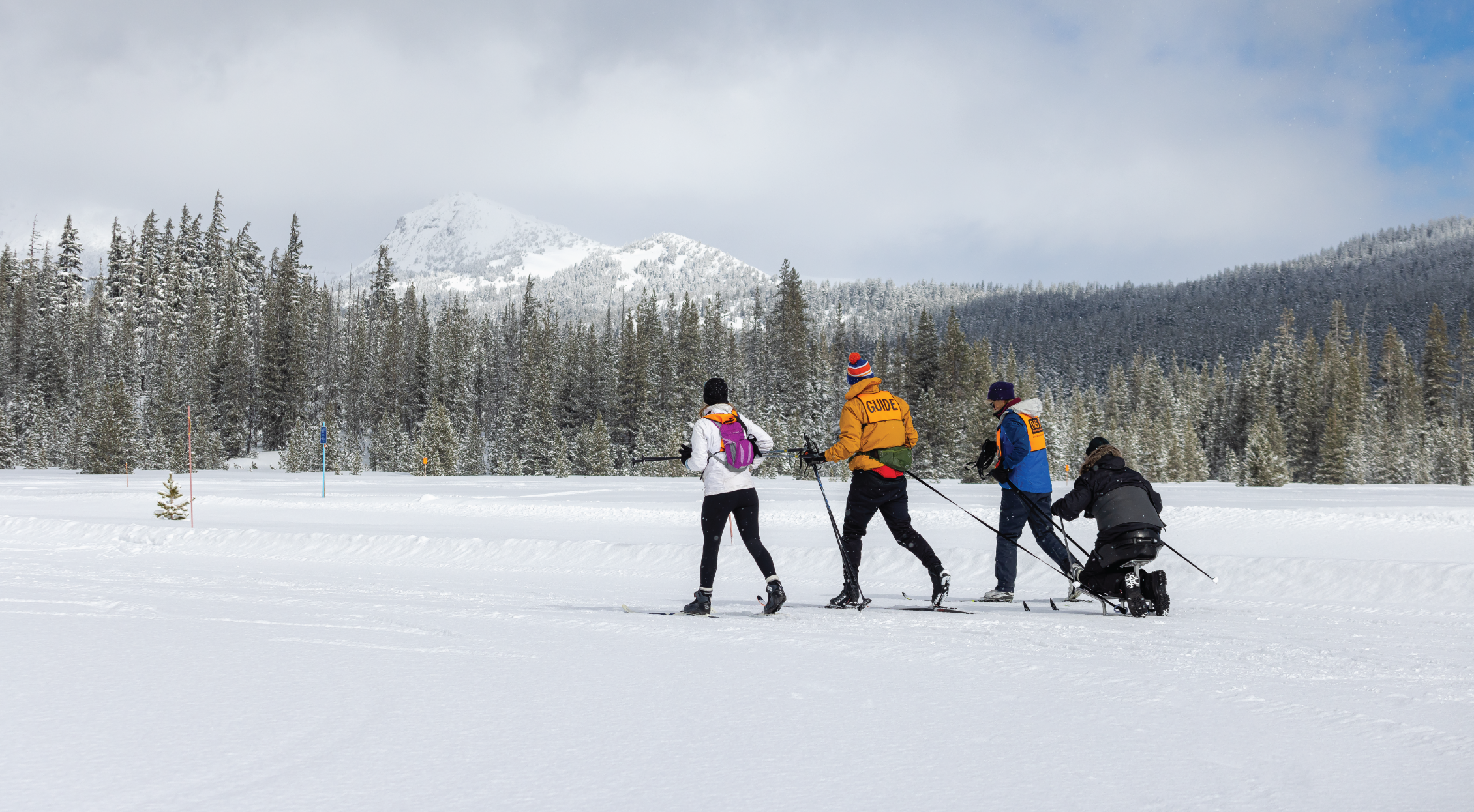 Nordic Skiing, three guides instruct a nordic sit skier on equipment use
