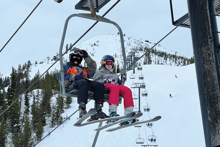 two CamPAH participants on a 2 seat lift. the image is taken from below the lift. Mountain summit is visible in the background