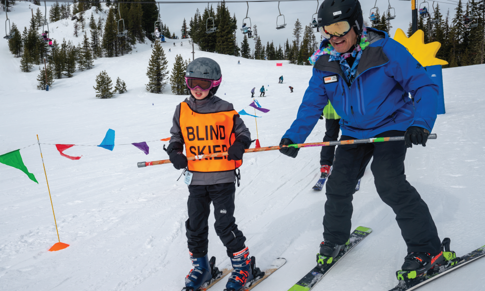 Young athlete who is visually impaired skis down the hill with an OAS instructor
