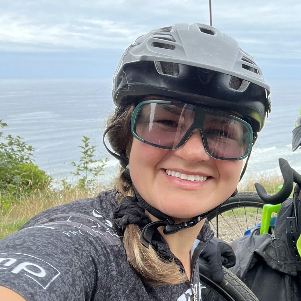 Hayley wearing light tinted sunglasses, hair in a braid with a grey helmet.