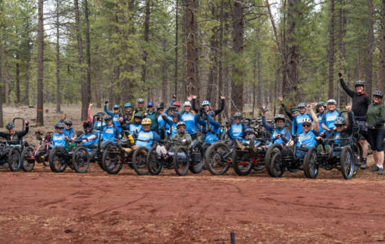 20 athletes in aMTBs and OAS volunteers and staff rally together in a group photo with tall pines lining their background