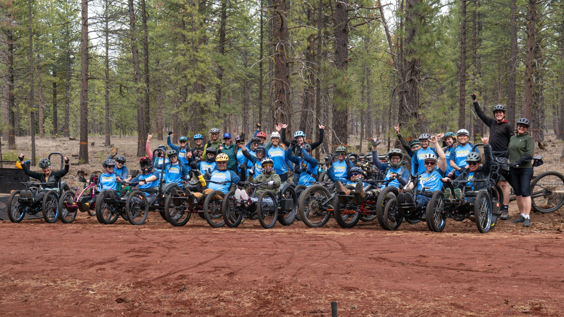 20 athletes in aMTBs and OAS volunteers and staff rally together in a group photo with tall pines lining their background