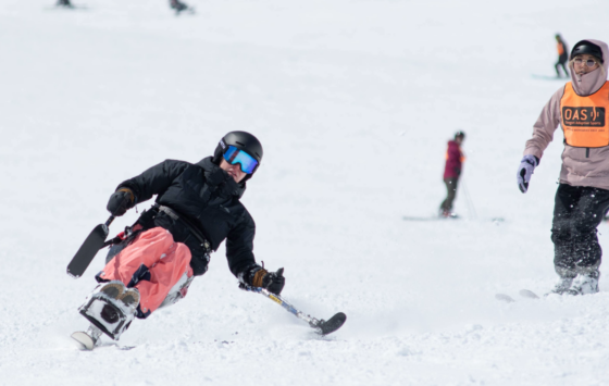 Joanna in her sit-ski comes down the slope unassisted with a few 2-track skiers visible from behind