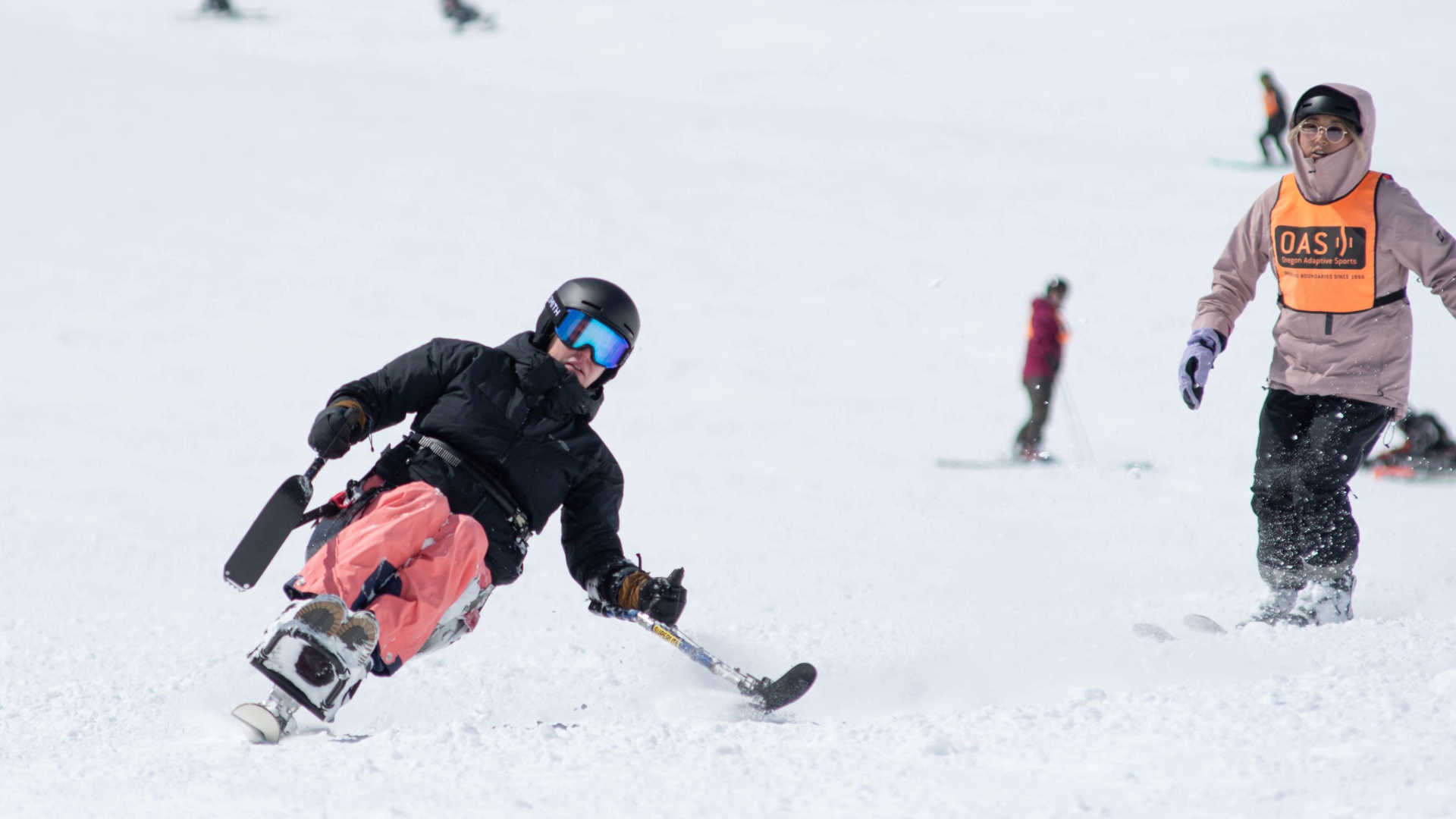 Joanna in her sit-ski comes down the slope unassisted with a few 2-track skiers visible from behind