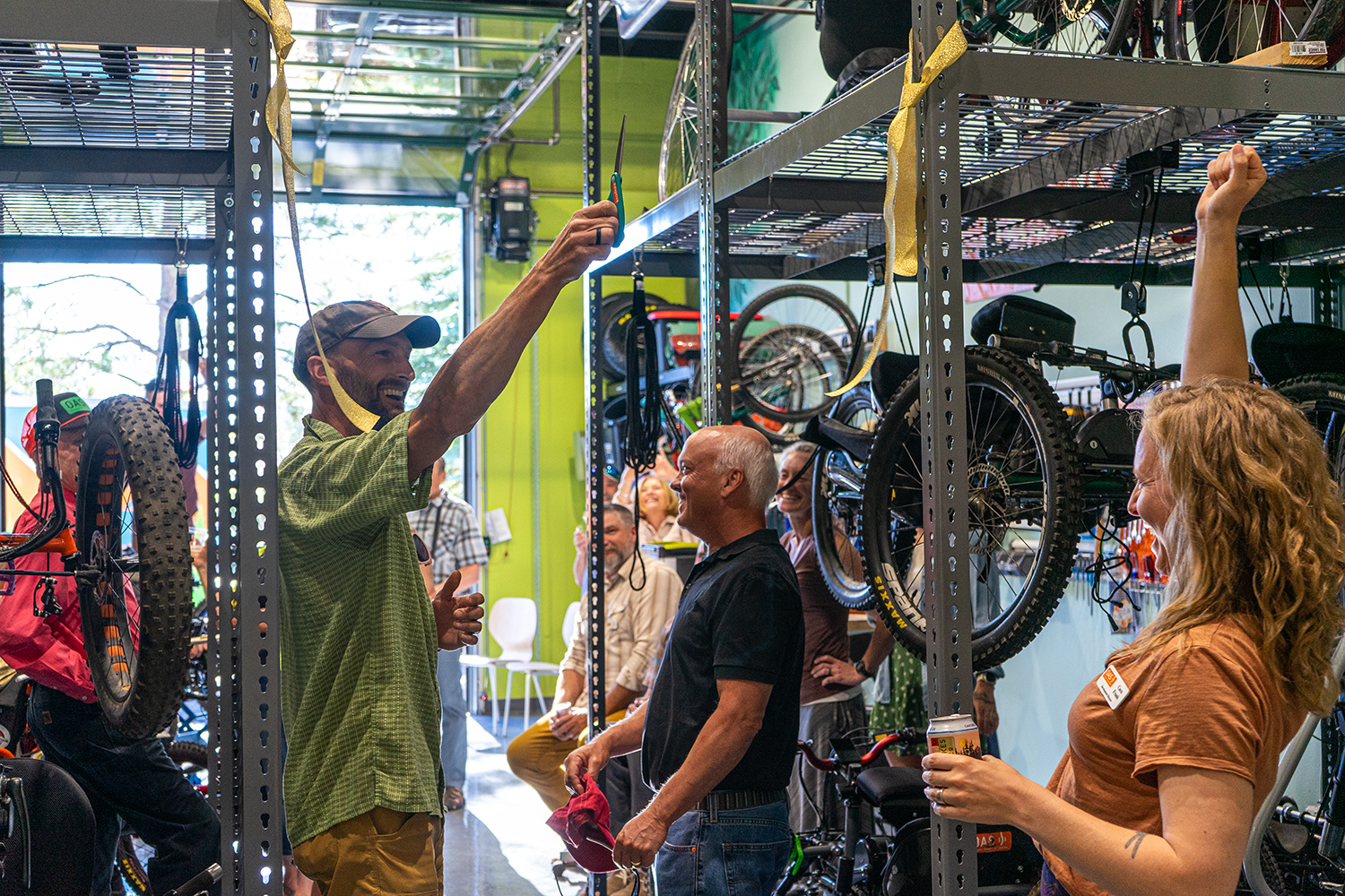 Jeremy Fox in a green polo shirt, uses scissors to cut a ribbon between two bike storage shelfs in celebration of the new space. Others around cheer