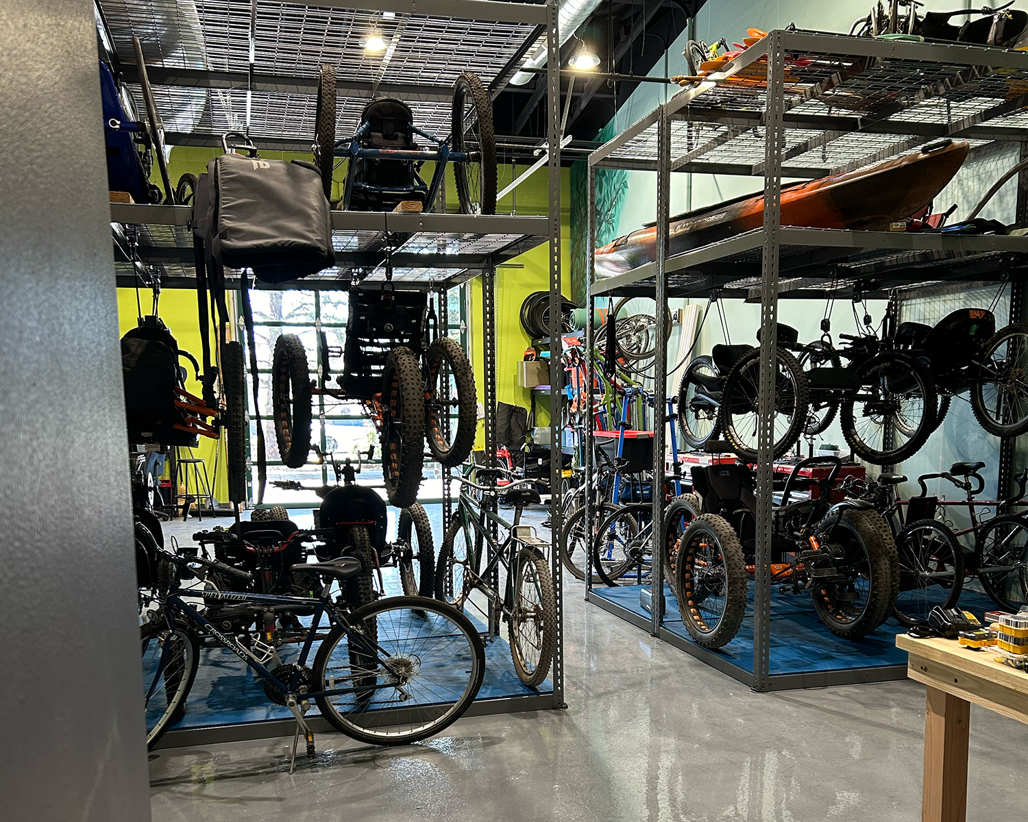 garage bay with large shelfs that are able to store bikes below and above each other with additional room for kayaks on top. open space beyond the shelfs is visible with a clear glass automatic garage door out the back