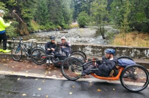 stopped along a bridge on a cloudy, rainy day the OAS crew takes a break with their bikes beside them.