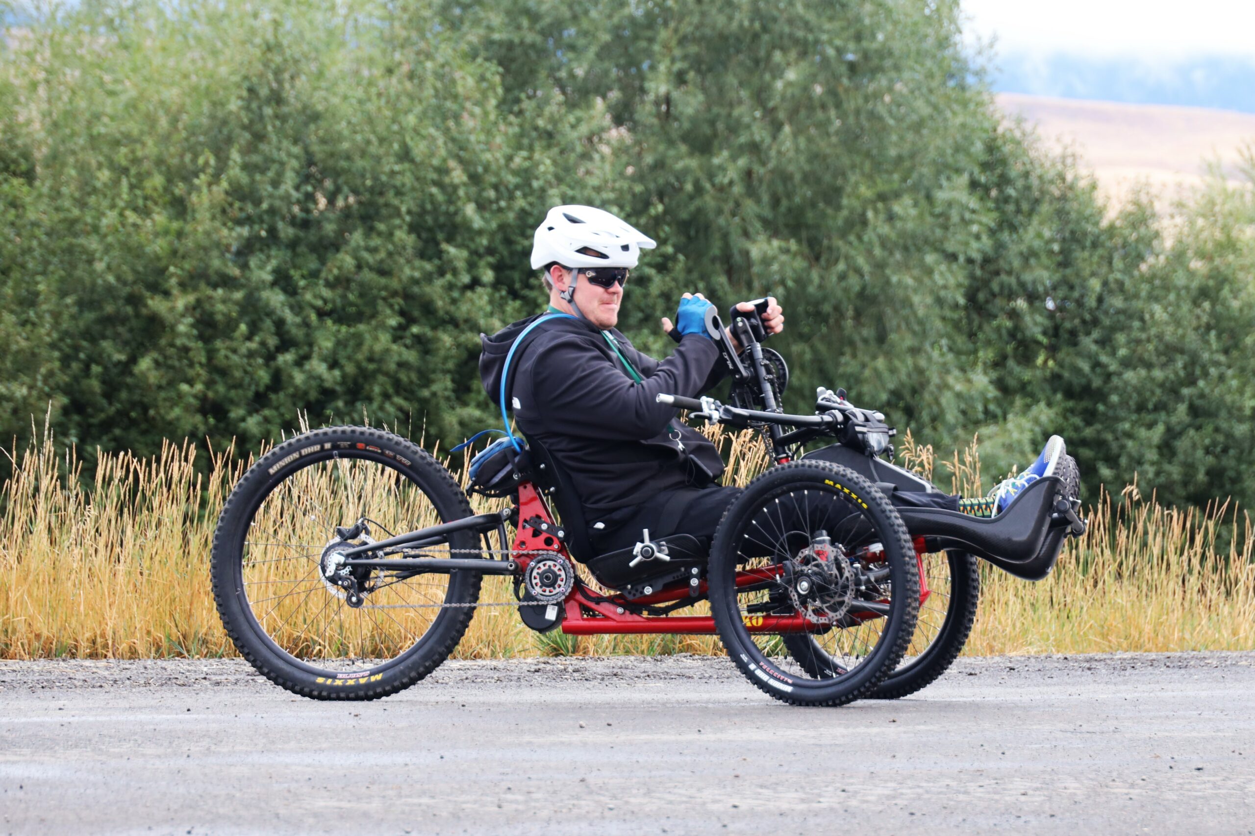 On the road is a male athlete in a handcycle with clear, cloudy weather