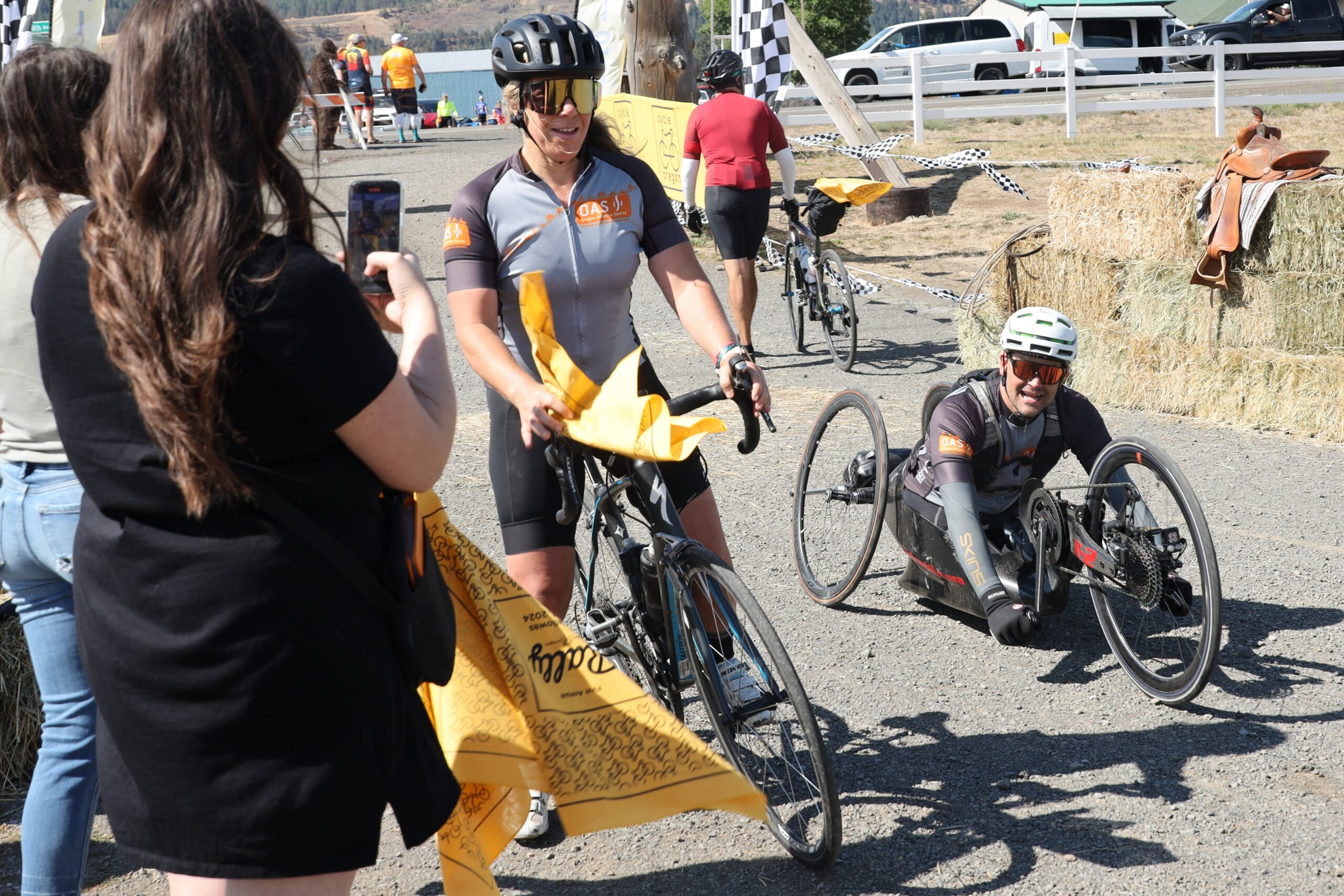 An OAS staff member on a bike and an athlete in a handcycle receive yellow "Cycle Oregon, the Rally" bandanas at having finished the event