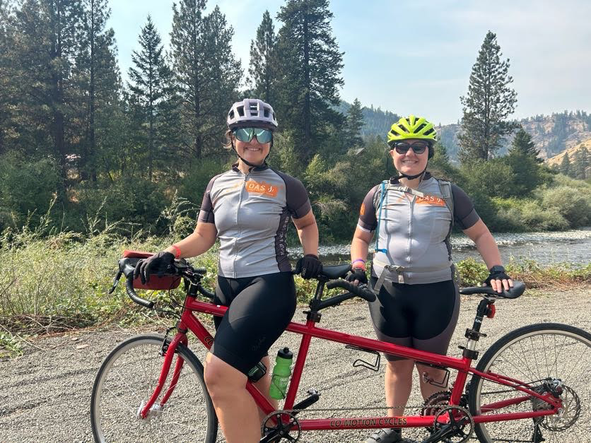 A bright red tandem cycle is featured with an OAS staff member at the front with an athlete at the rear. 