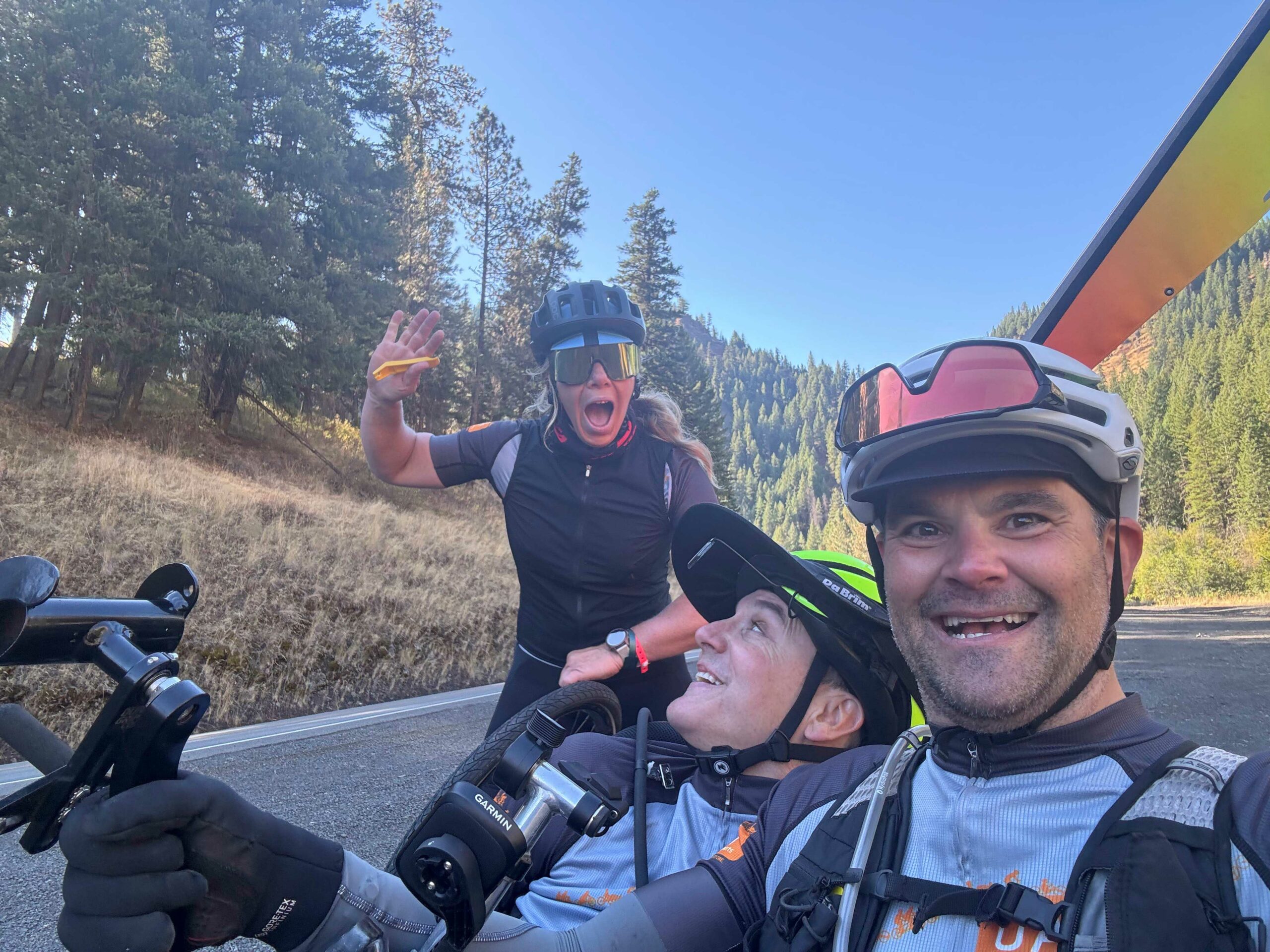 A trio selfie with two athletes in handcycles and an OAS staff member waving from the back