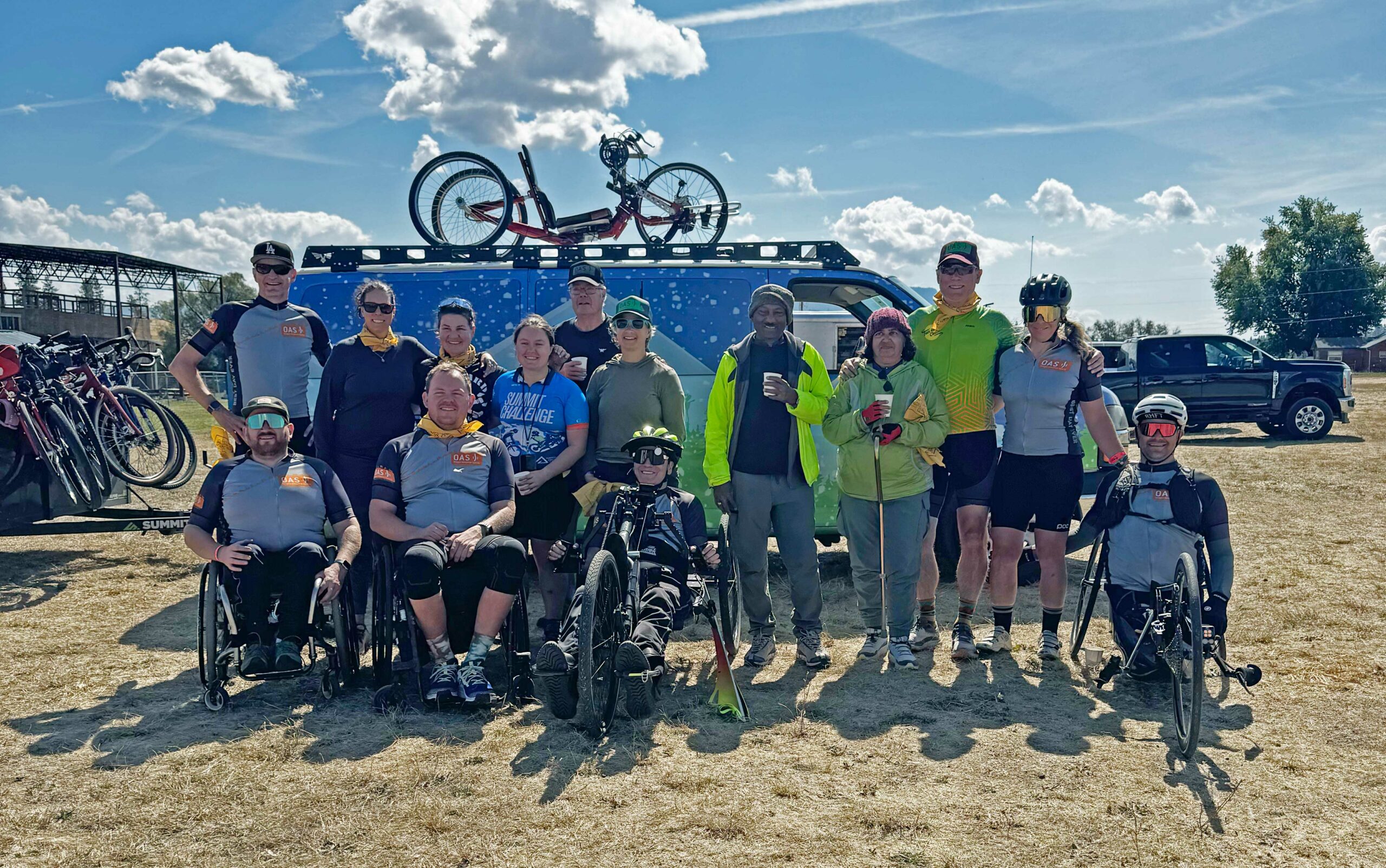 A group photo on the grass with the entire OAS crew and the OAS van behind them with a handcycle on the top