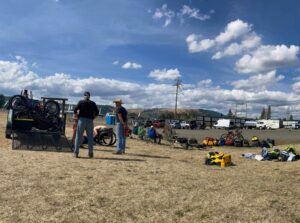 A wide photo showing a staging area at the beginning/end of a cycling day with the OAS trailer and gear strewn about.