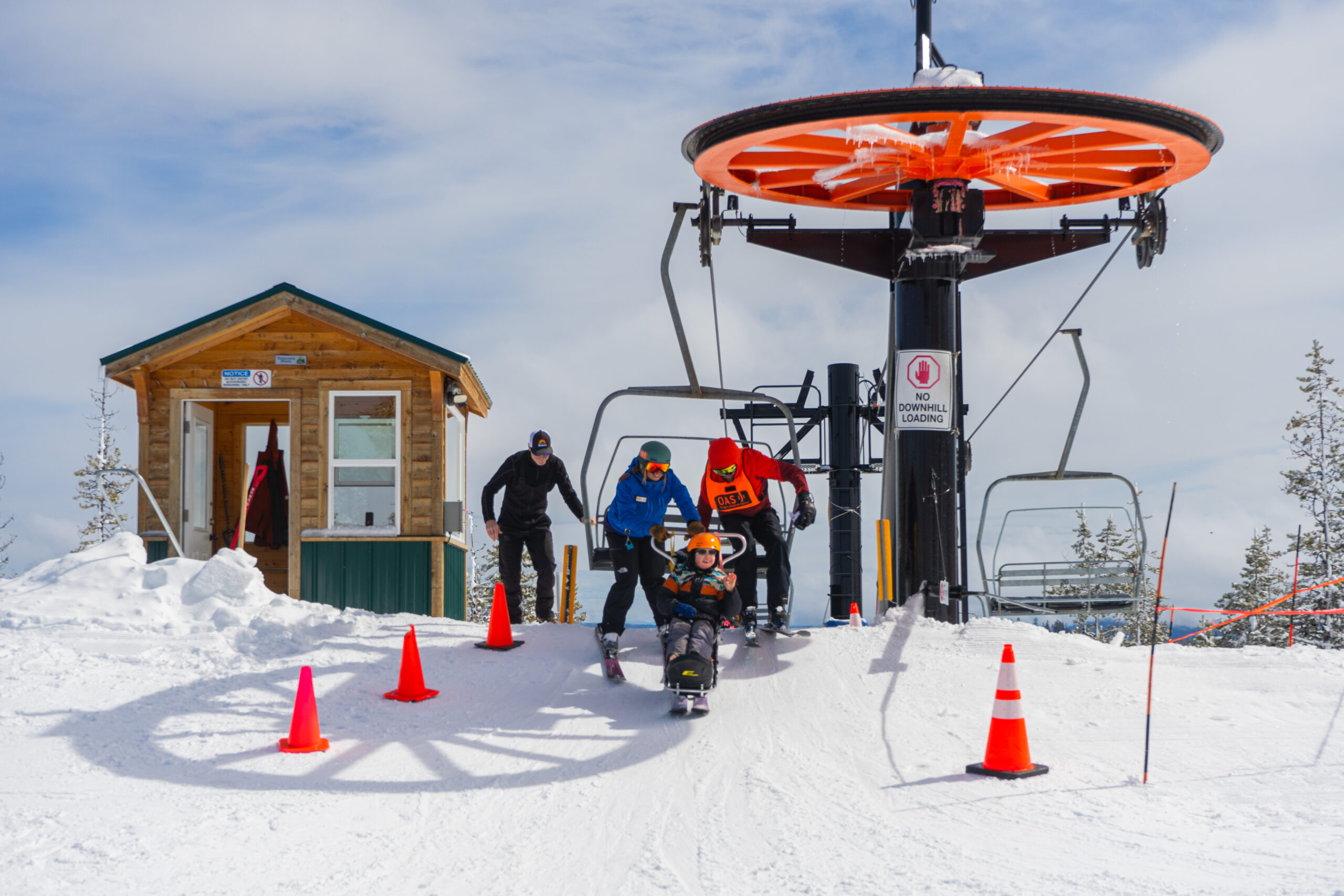 A child in a sit-ski unloading from a chairlift with assistance of an OAS instructor and volunteer