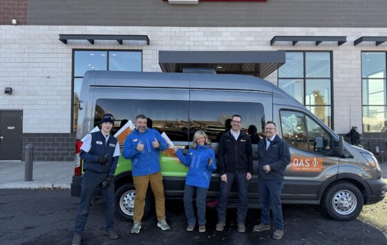 A van with OAS on it and new tires, Les Schwab employees with two OAS staff stand in front of van smiling outside