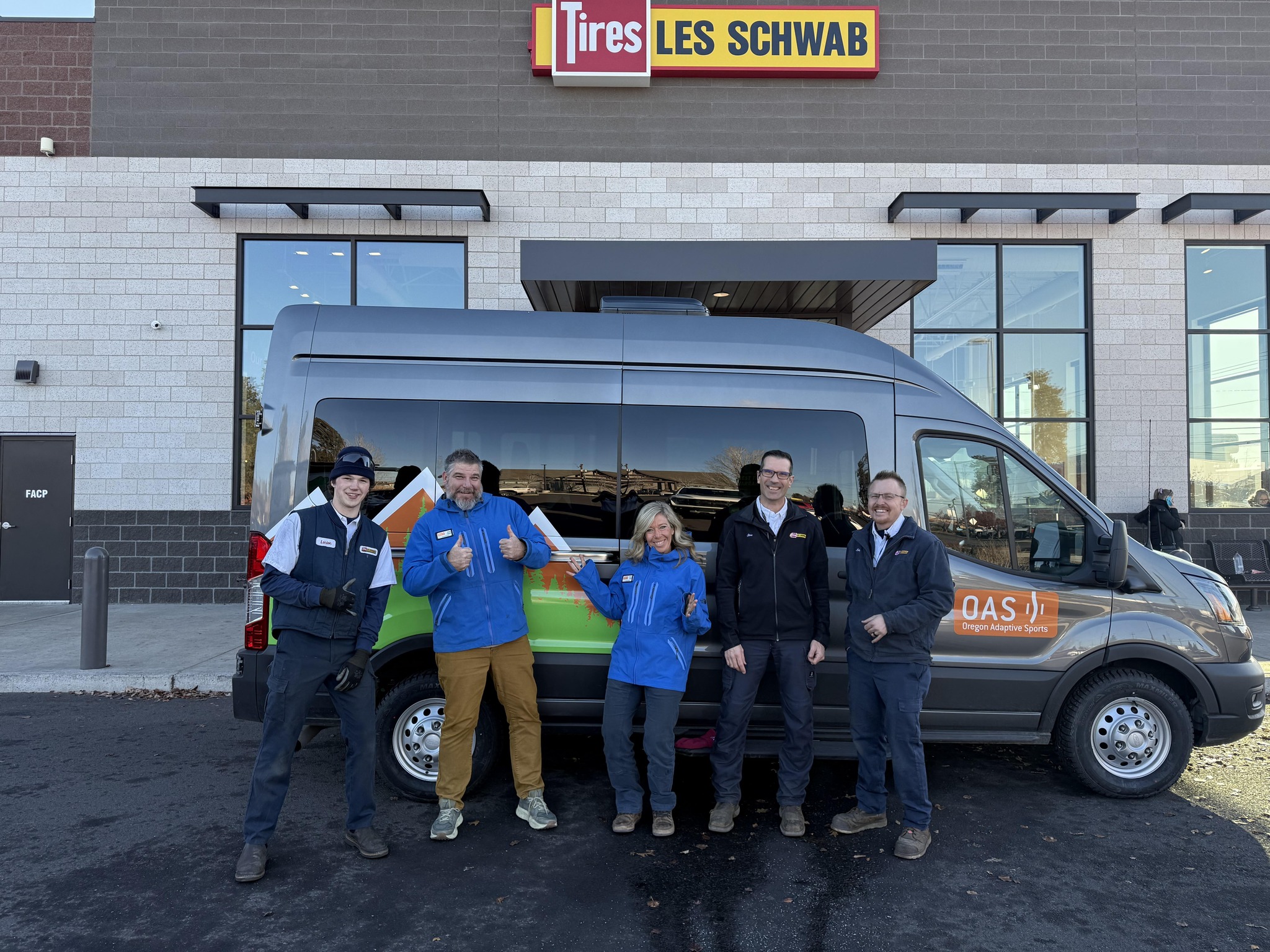 A van with OAS on it and new tires, Les Schwab employees with two OAS staff stand in front of van smiling outside