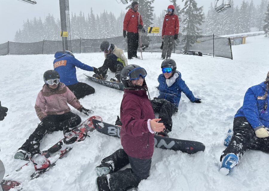 Snowy conditions surround a group of athletes and OAS volunteers as they strap into snowboards