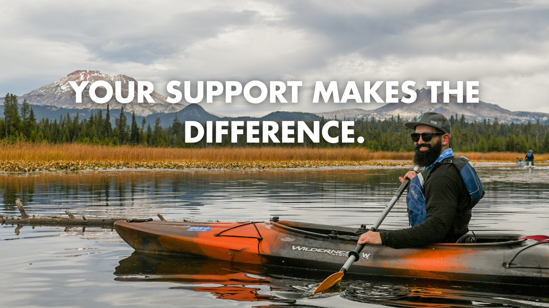A person paddling a single kayak during O-A-S paddling programs.He looks directly at the camera, with a smile framed by a dark thick beard. text: Your support makes the difference"