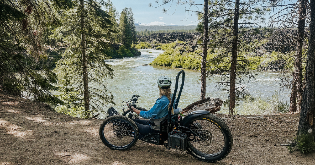 Sophie, a woman with long blonde hair, looks over a rapid from her bike. 