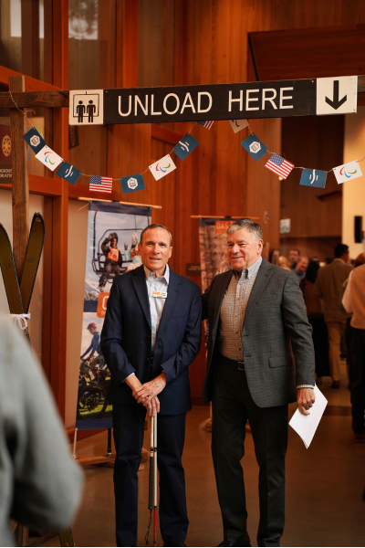 Two men wearing formal pantsuits pose for a photo under the "Unload here" sign in the entry way.