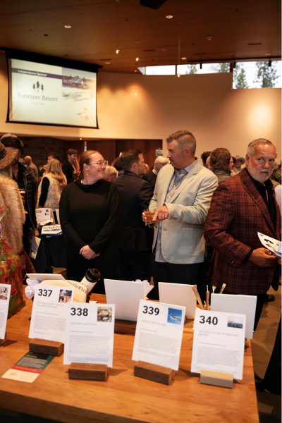 a man wearing a grey sport coat signs with a woman wearing all black. They stand over the auction display and are pointing at a package.