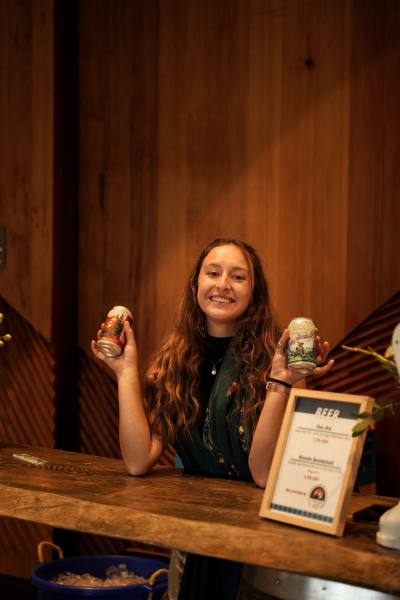 Beertender Leta, a woman with long brown hair, shows the two beer options for the night, one in each hand.