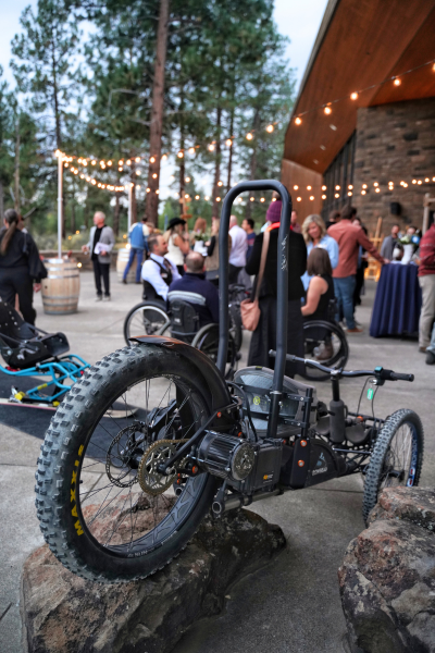 am adaptive mountain bike is propped up on a rock with blurry people socializing in the background.