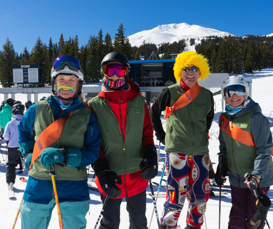 four people wearing green gear fix vests and fake mustaches with orange ski for all sashes on.