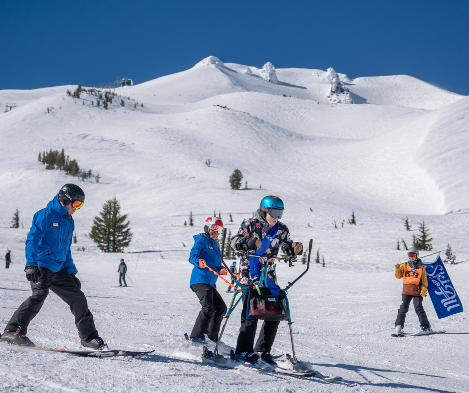 a person in a colorful button down shirt skis with a slider, while being tethered by an O-A-S instructor in a blue jacket.