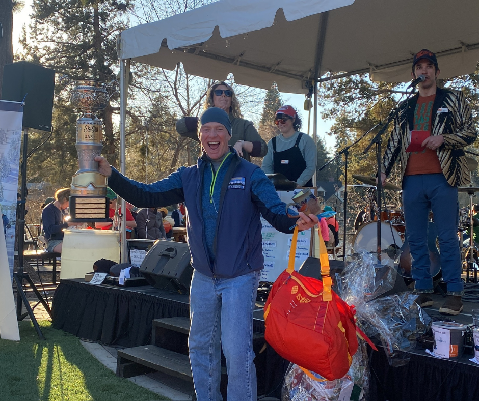 a man wearing jeans and a blue puffy celebrates after winning a prize at the Ski For All after party