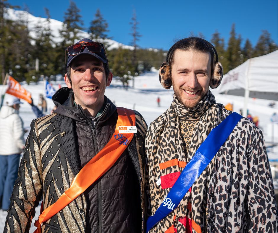 two men pose together for a photo: on the left, Pat wears a gold sparkly sport coat, orange sash, and black hat. On the right, jesse wears head to toe cheetah print and a blue sash.