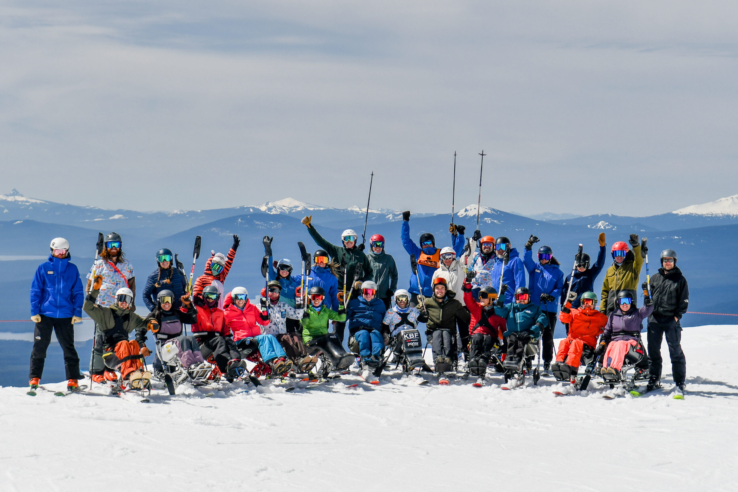 A large group of people on sit skis and standing raise their arms in the air 