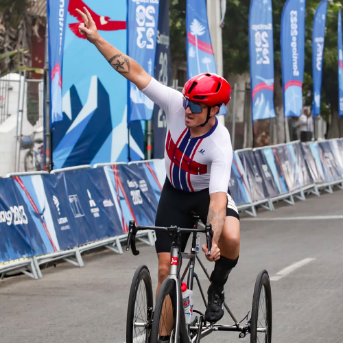 Dennis connors raises one arm in the air in triumph as he crosses the finish line on his road cycle. 