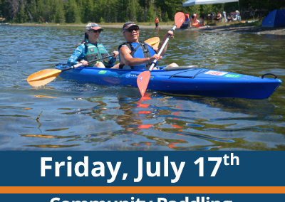 Friday, July 17th. Community Paddling. Paddle and Play. Two people paddle a blue tandem kayak across a lake, each holding a double-bladed paddle, with a forested shoreline