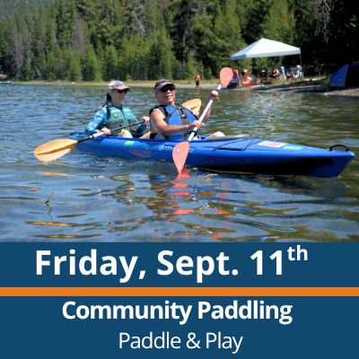 Friday, Sept. 11th. Community Paddling. Paddle and Play. Two people paddle a blue tandem kayak across a lake, each holding a double-bladed paddle, with a forested shoreline