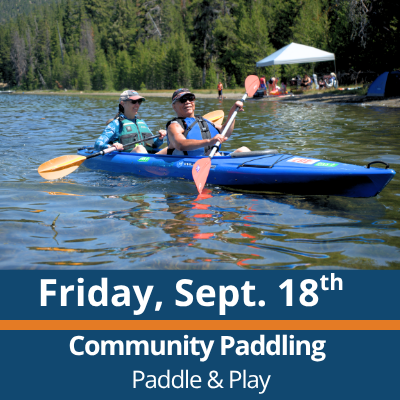 Friday, Sept. 18th. Community Paddling. Paddle and Play. Two people paddle a blue tandem kayak across a lake, each holding a double-bladed paddle, with a forested shoreline