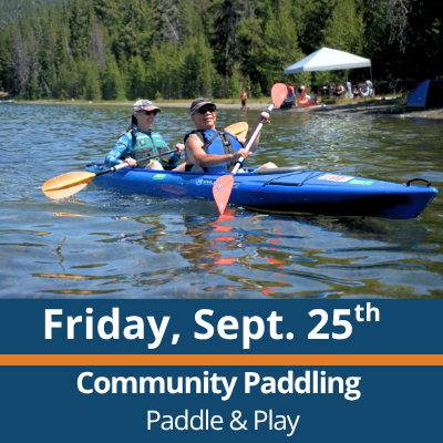 Friday, Sept. 25th. Community Paddling. Paddle and Play. Two people paddle a blue tandem kayak across a lake, each holding a double-bladed paddle, with a forested shoreline