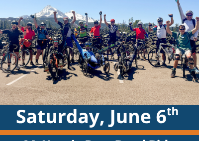 Saturday, June 6th. McKenzie Pass Road Ride. Sisters, OR. A large group of cyclists and handcyclists gather on a paved road with their bikes, many raising their arms, with mountains and trees visible in the background.