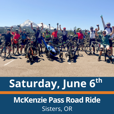 Saturday, June 6th. McKenzie Pass Road Ride. Sisters, OR. A large group of cyclists and handcyclists gather on a paved road with their bikes, many raising their arms, with mountains and trees visible in the background.