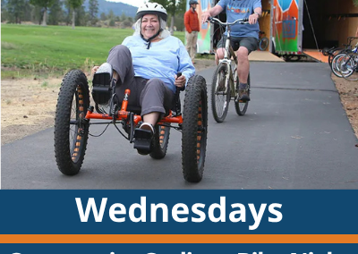 Wednesdays. Community Cycling Bike Night. Pine Nursery Park. A person smiles while riding a three-wheeled bicycle on a paved path, with another person riding a bike behind them and a trailer and trees visible in the background.